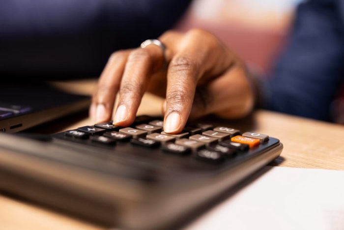 Hand using a calculator beside a laptop